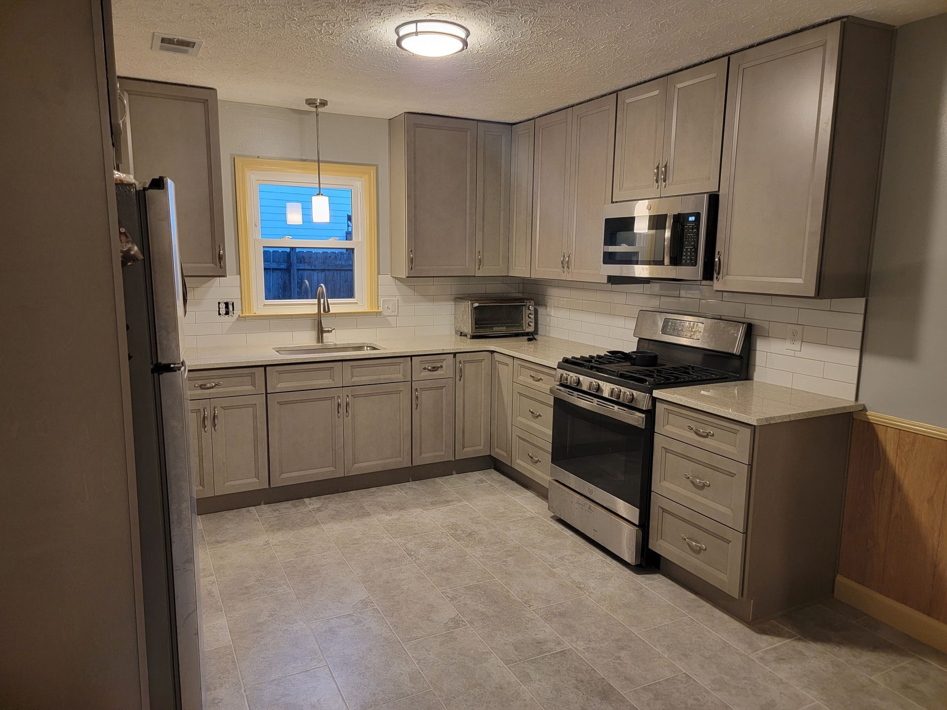 Bright modern kitchen with white cabinets, island, pendant lights, and dark wood floors opening to a dining area