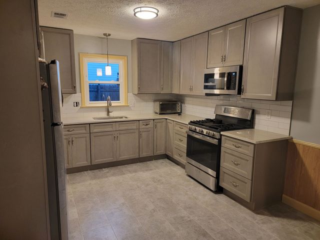 Compact modern kitchen with gray cabinets, stainless steel appliances, and a window over the sink.