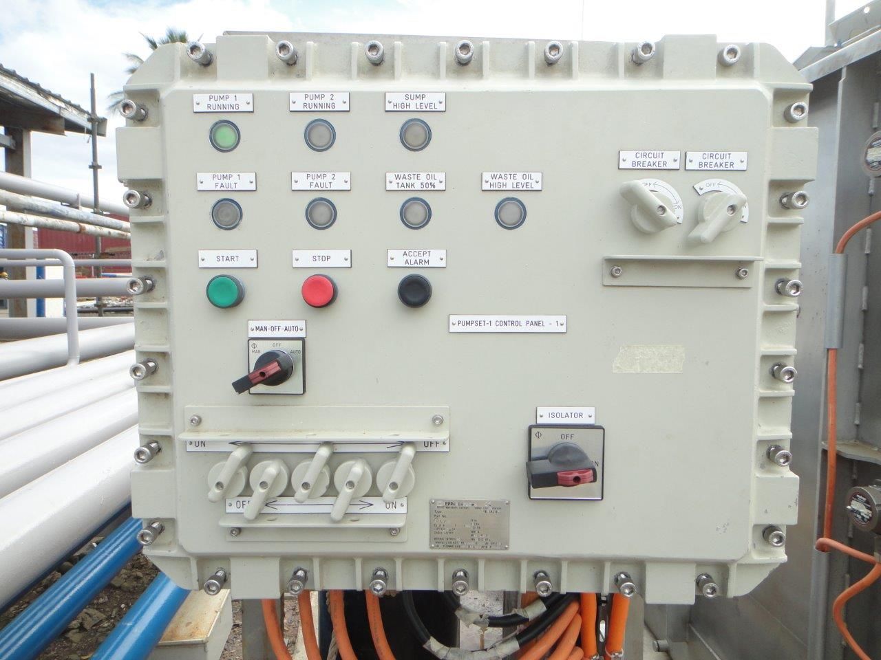 Gray electrical control box with lights, switches, and wiring outdoors near pipes.