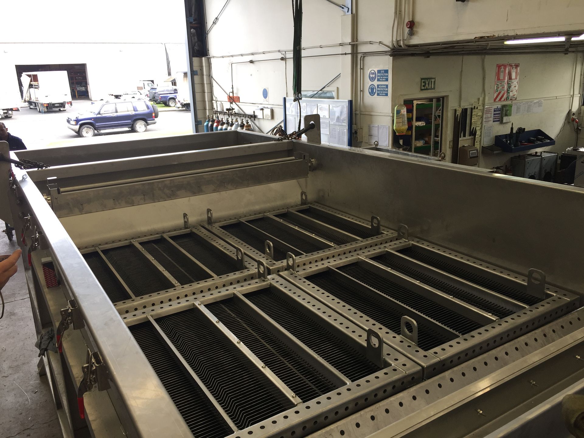 Large metal industrial container with rectangular compartments and internal grids, in a workshop setting.