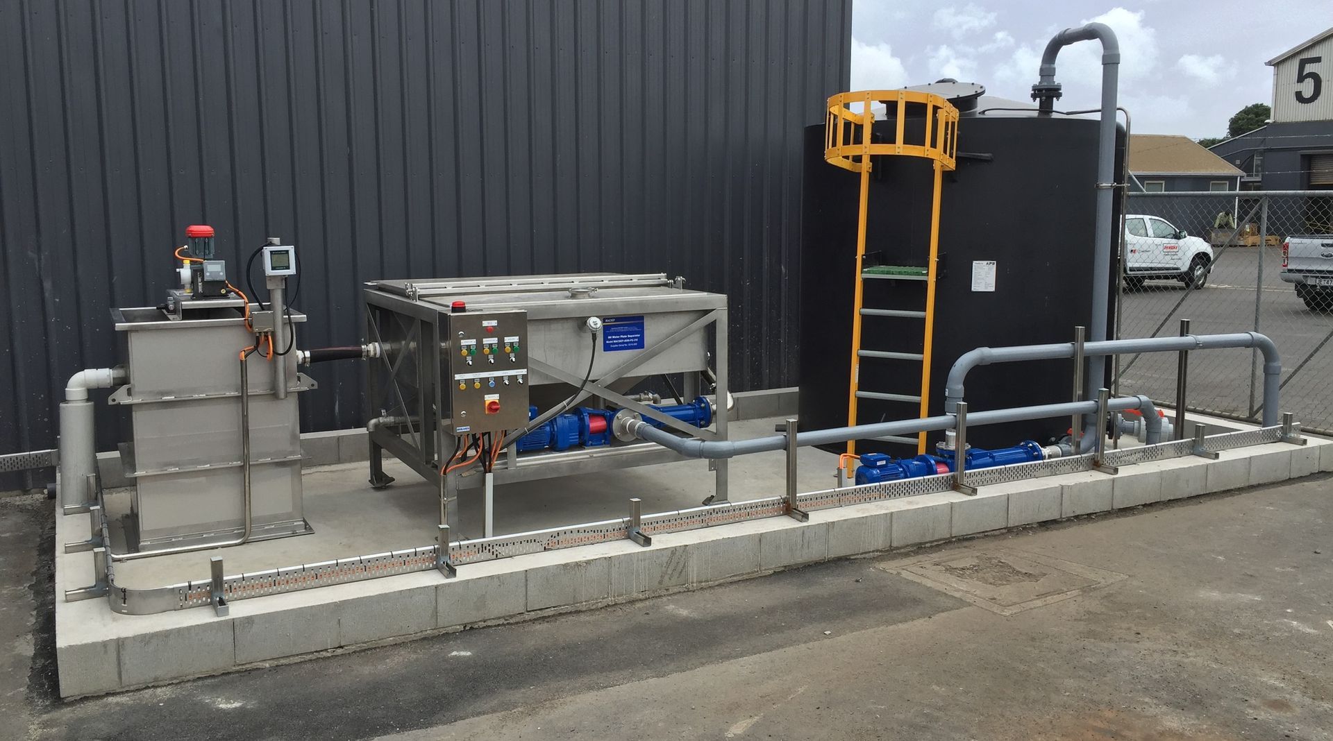 Industrial wastewater treatment system with tanks, pipes, and control panel outdoors.