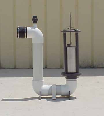White PVC pipe apparatus with metal components, likely for plumbing or water filtration, outdoors on a light surface.
