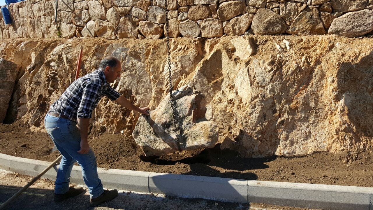 Ein Mann schaufelt Erde vor einer Steinmauer.