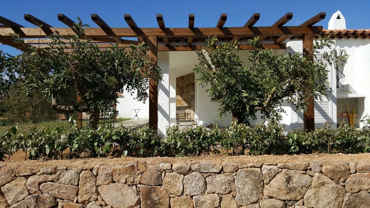 Ein weißes Haus mit einer Steinmauer und einer hölzernen Pergola