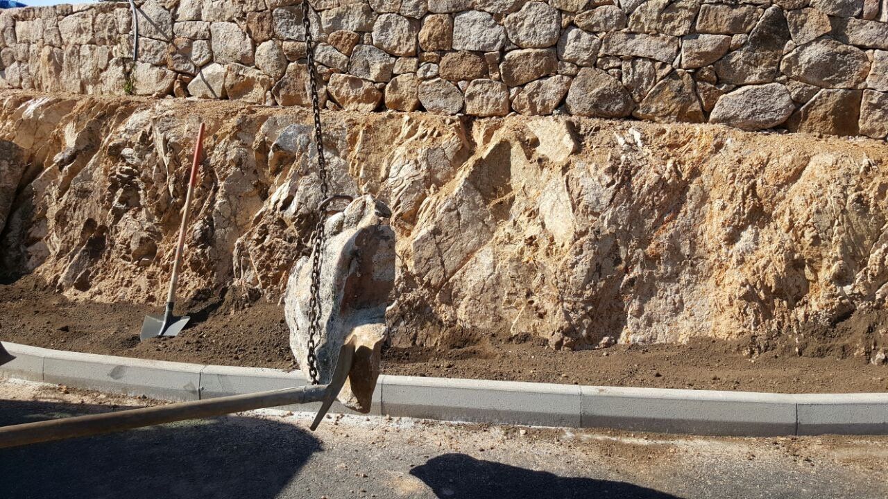 Eine Person gräbt vor einer Steinmauer ein Loch in den Boden.