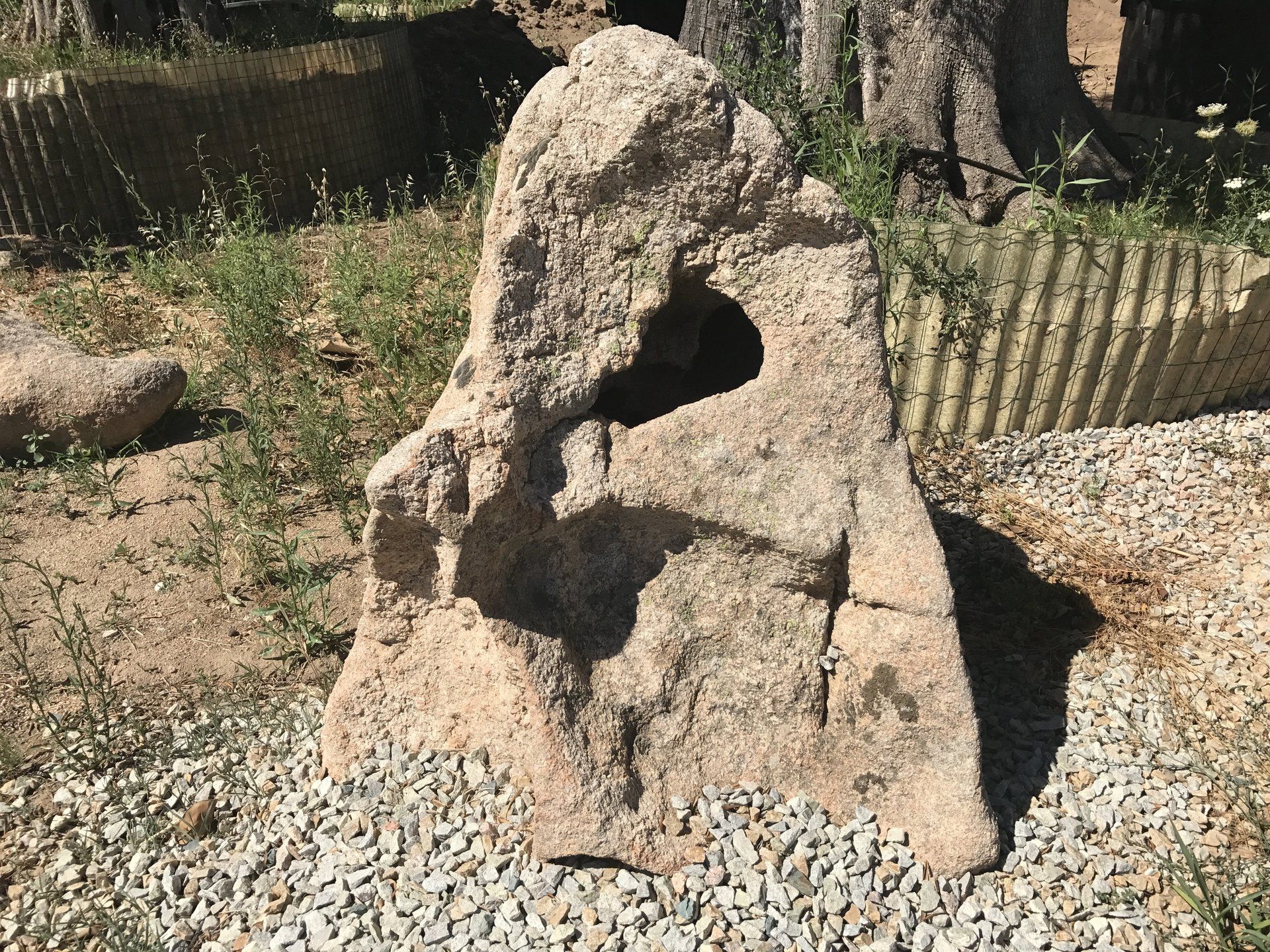 Ein großer Stein mit einem Loch darin liegt auf Kies.