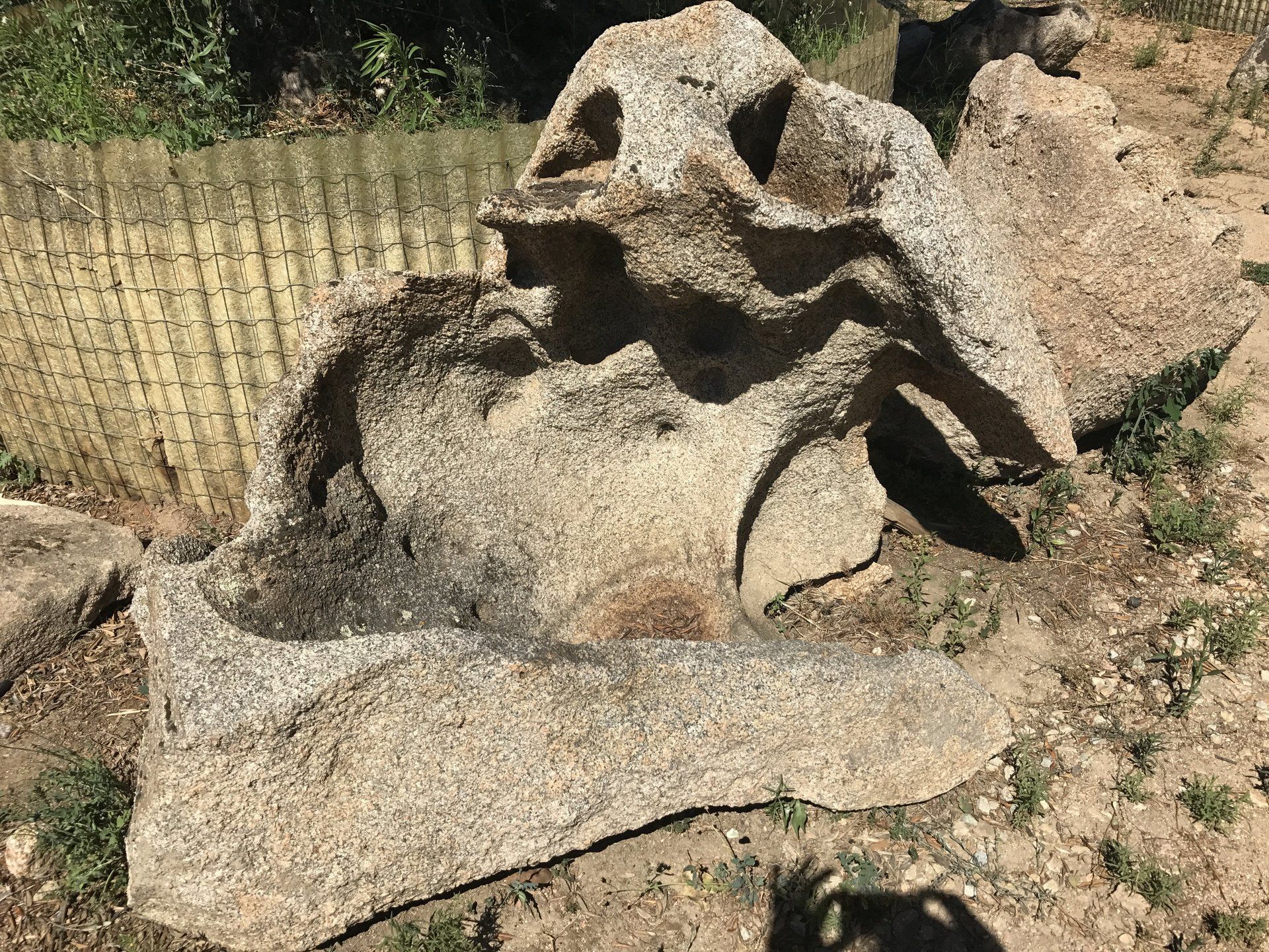 Ein großer Stein liegt im Dreck neben einem Zaun.