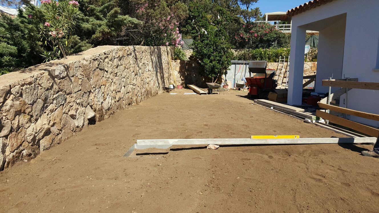 Un cortile con un muro di pietra e una casa bianca sullo sfondo.