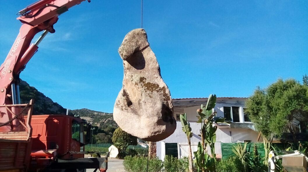 Vor einem Haus wird ein großer Fels von einem Kran angehoben.