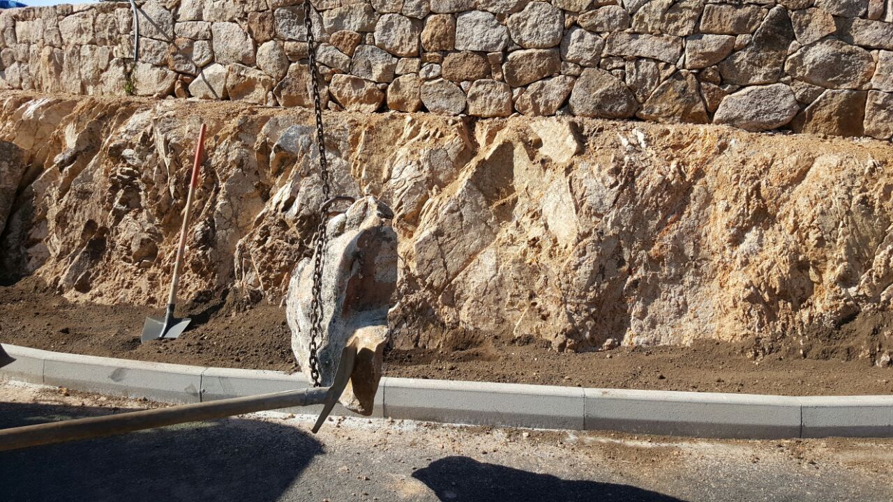 Eine Person gräbt vor einer Steinmauer ein Loch in den Boden.