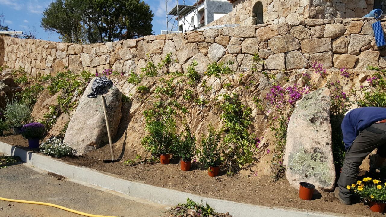 Ein Mann pflanzt Blumen vor einer Steinmauer.
