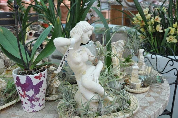 On a table surrounded by potted plants sits a statue of a woman.