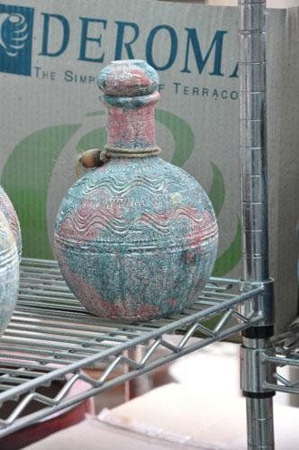 A bottle sits on a metal shelf in front of a cardboard box marked derom