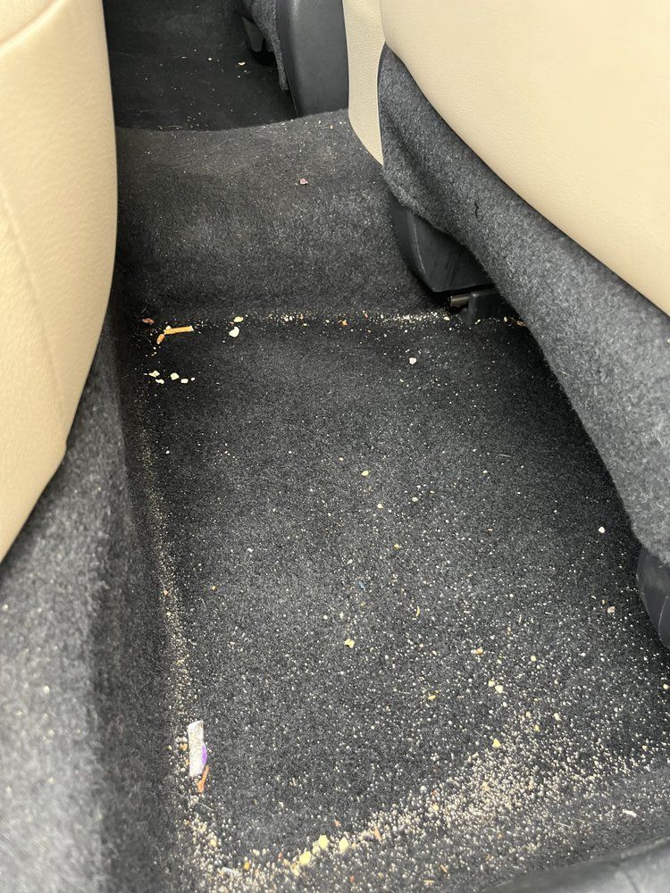 Dirty car floor mat with scattered debris between beige seats