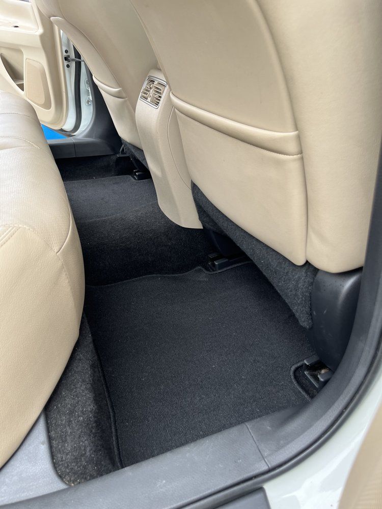 Carpeted back seat footwell of a car with beige seat backs and black floor mat