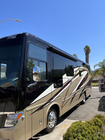 Black and tan motorhome parked on a sunny street with palm trees nearby