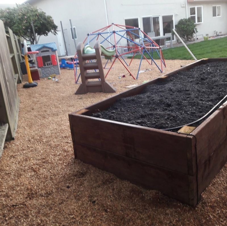 A wooden box filled with dirt sits in the middle of a playground