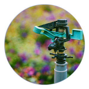 A green sprinkler is sitting in front of a field of flowers.