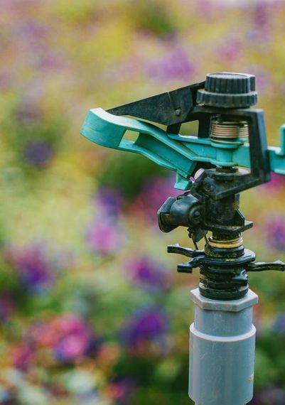 A close up of a sprinkler in a garden with flowers in the background.