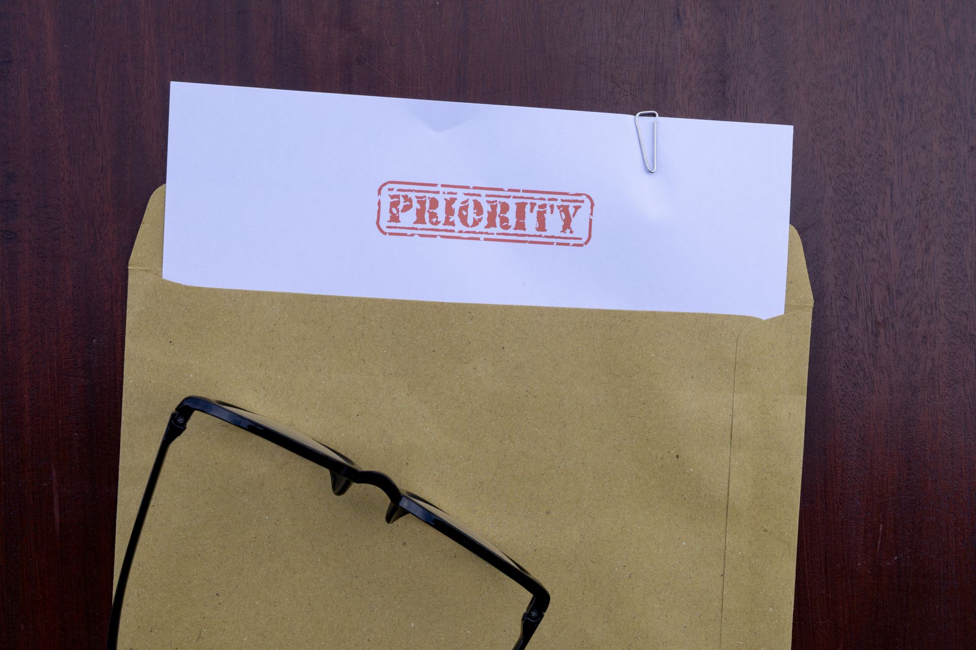 Black eyeglasses on a tan folder with a white tab labeled in red, against a dark wood background