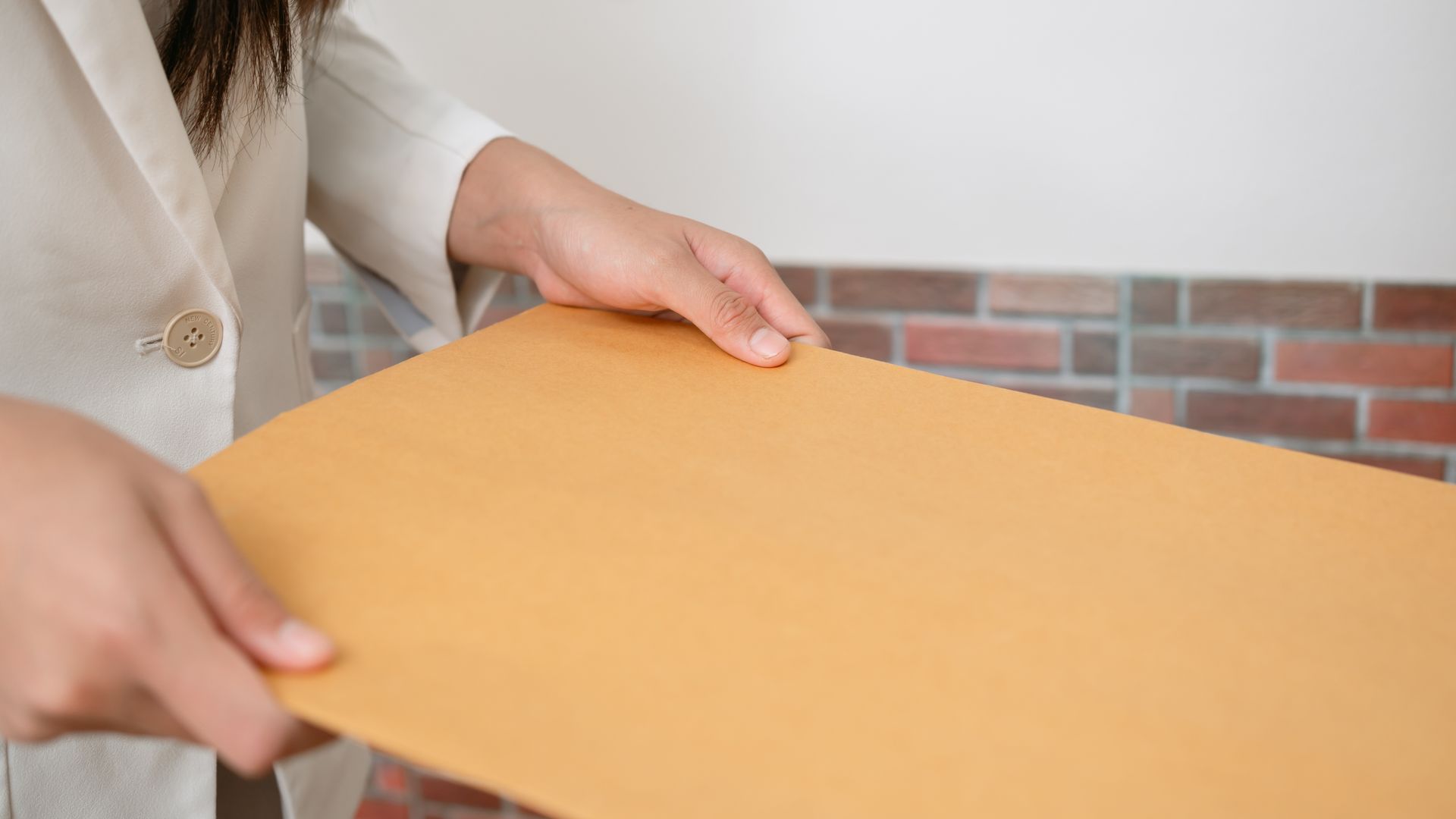 Person holding a large cardboard box in a room with a brick wall background