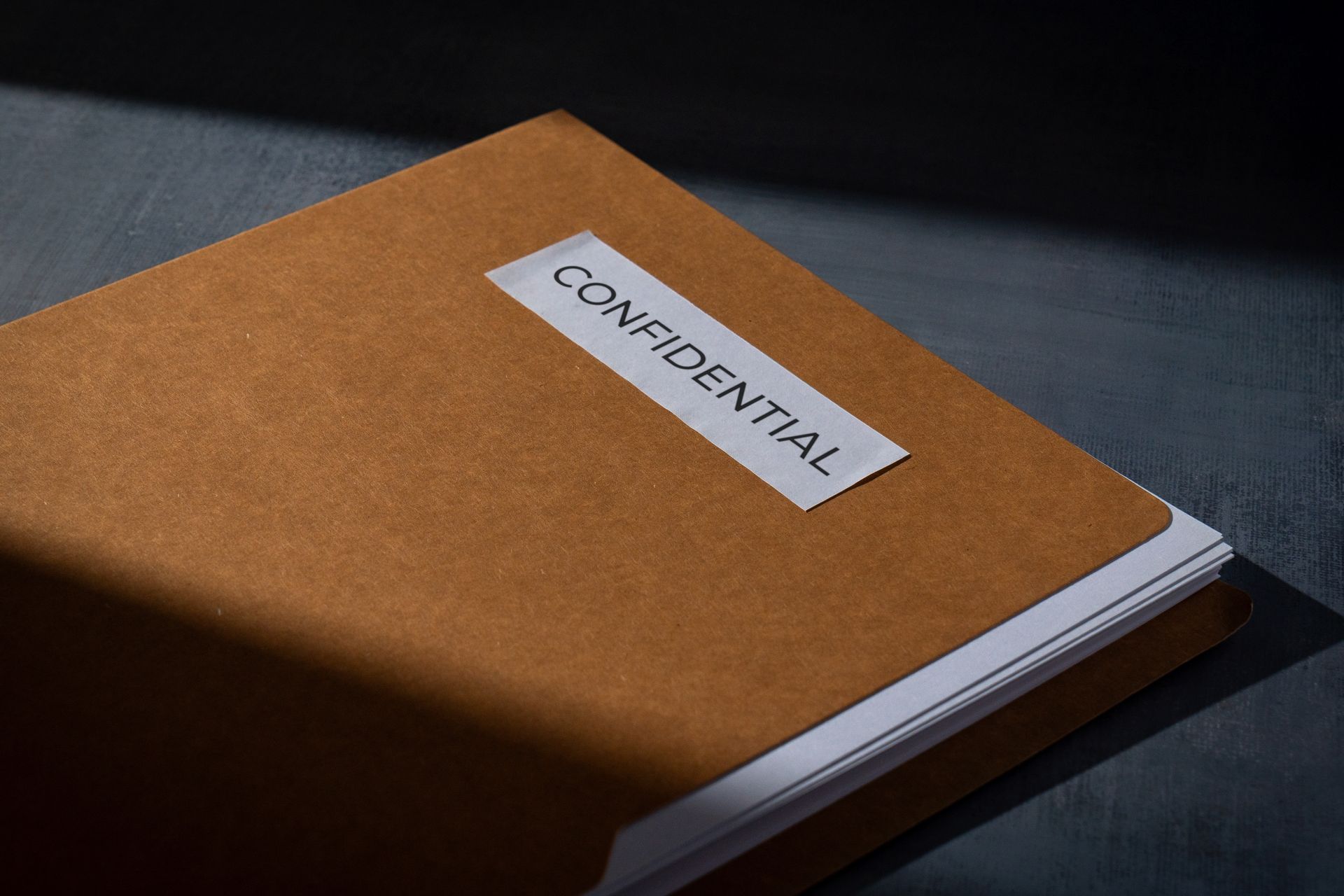 Brown notebook with a white CONFIDENTIAL label on a dark surface