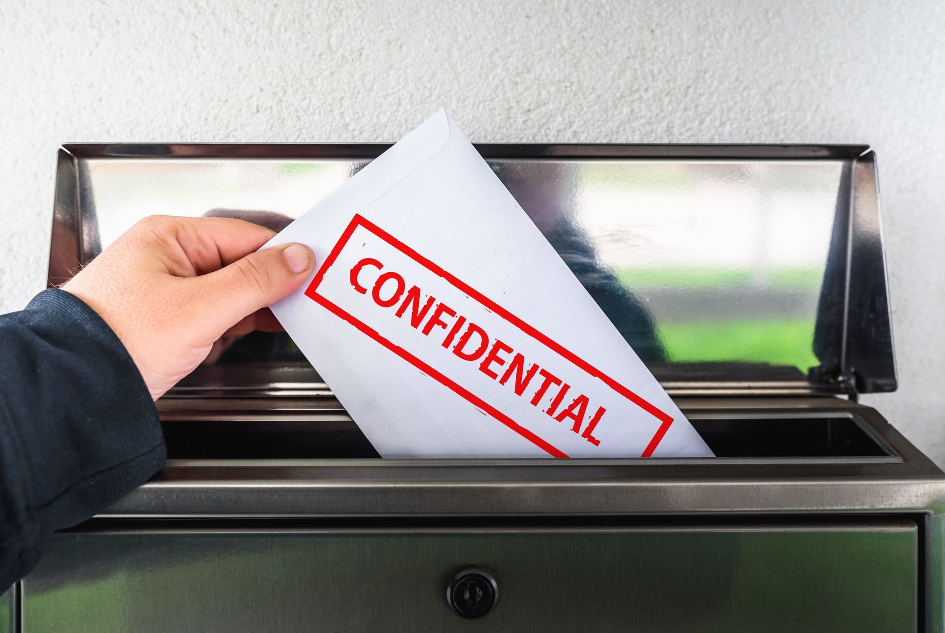 Hand inserting a confidential envelope into a metal mail slot