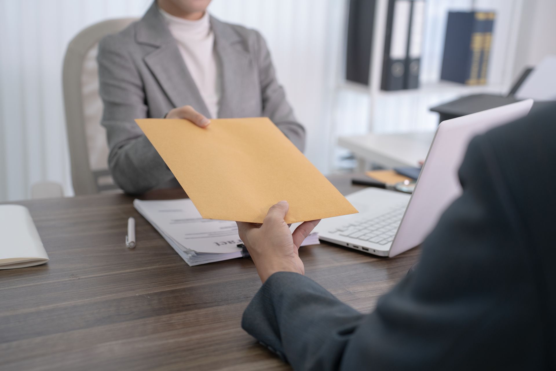 Person handing a tan folder across a desk in an office meeting