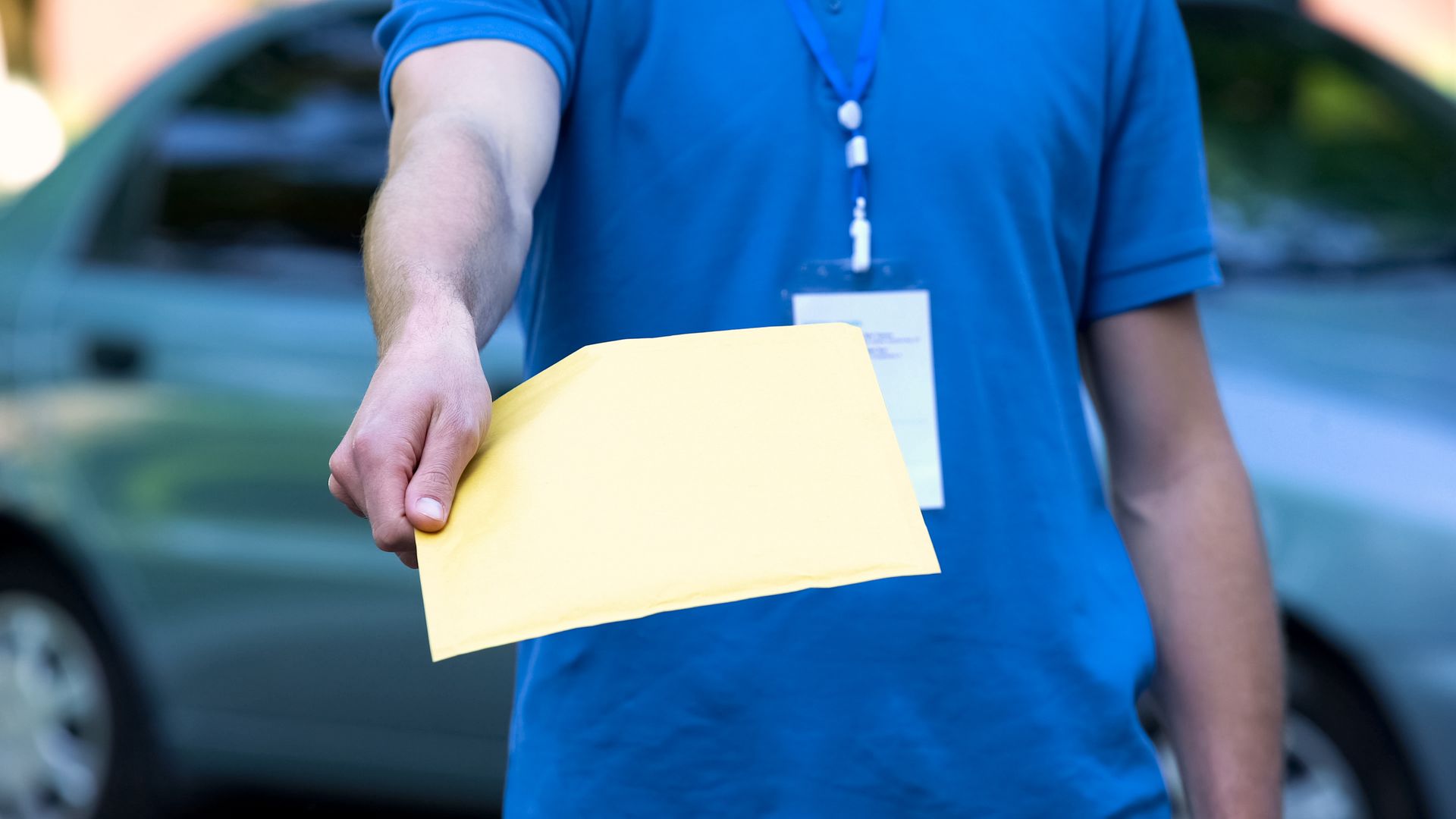 Person in a blue shirt holding out a yellow envelope outdoors