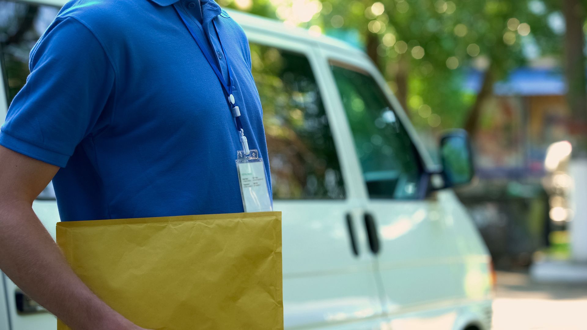 Delivery worker holding a yellow parcel beside a white van outdoors