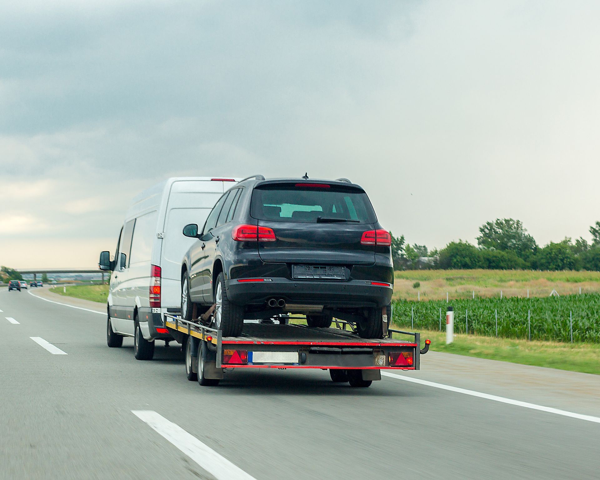 Black SUV and white van loaded on a trailer driving on a highway