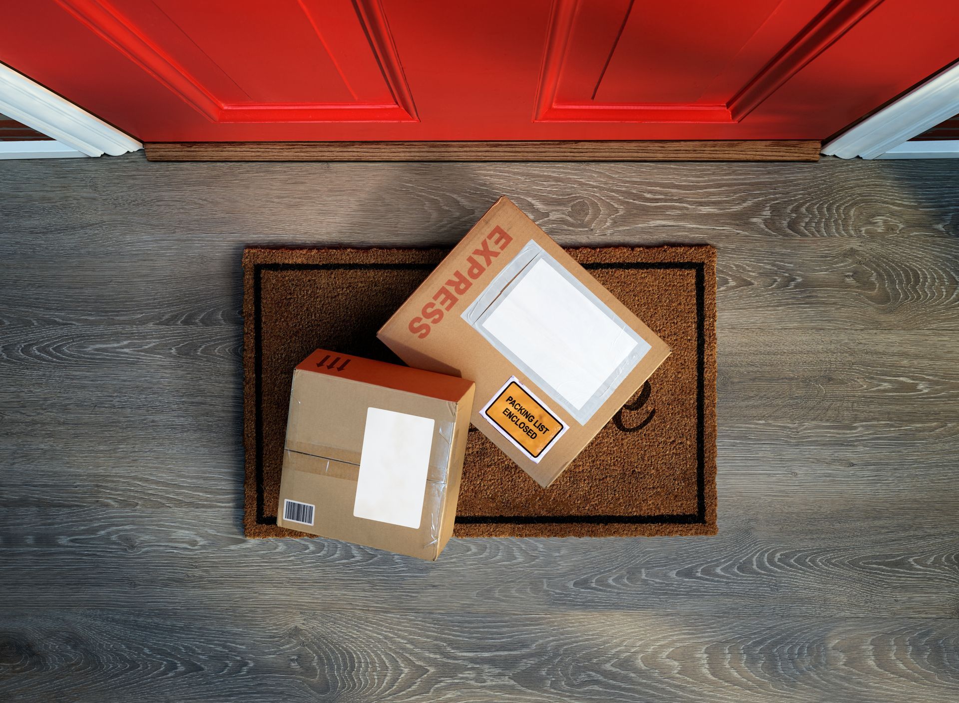 Two cardboard packages on a doormat by a red front door