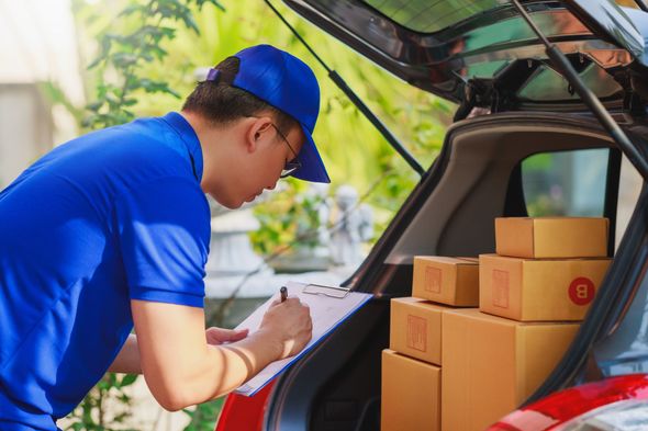 Delivery worker in blue uniform loading cardboard boxes into a car trunk