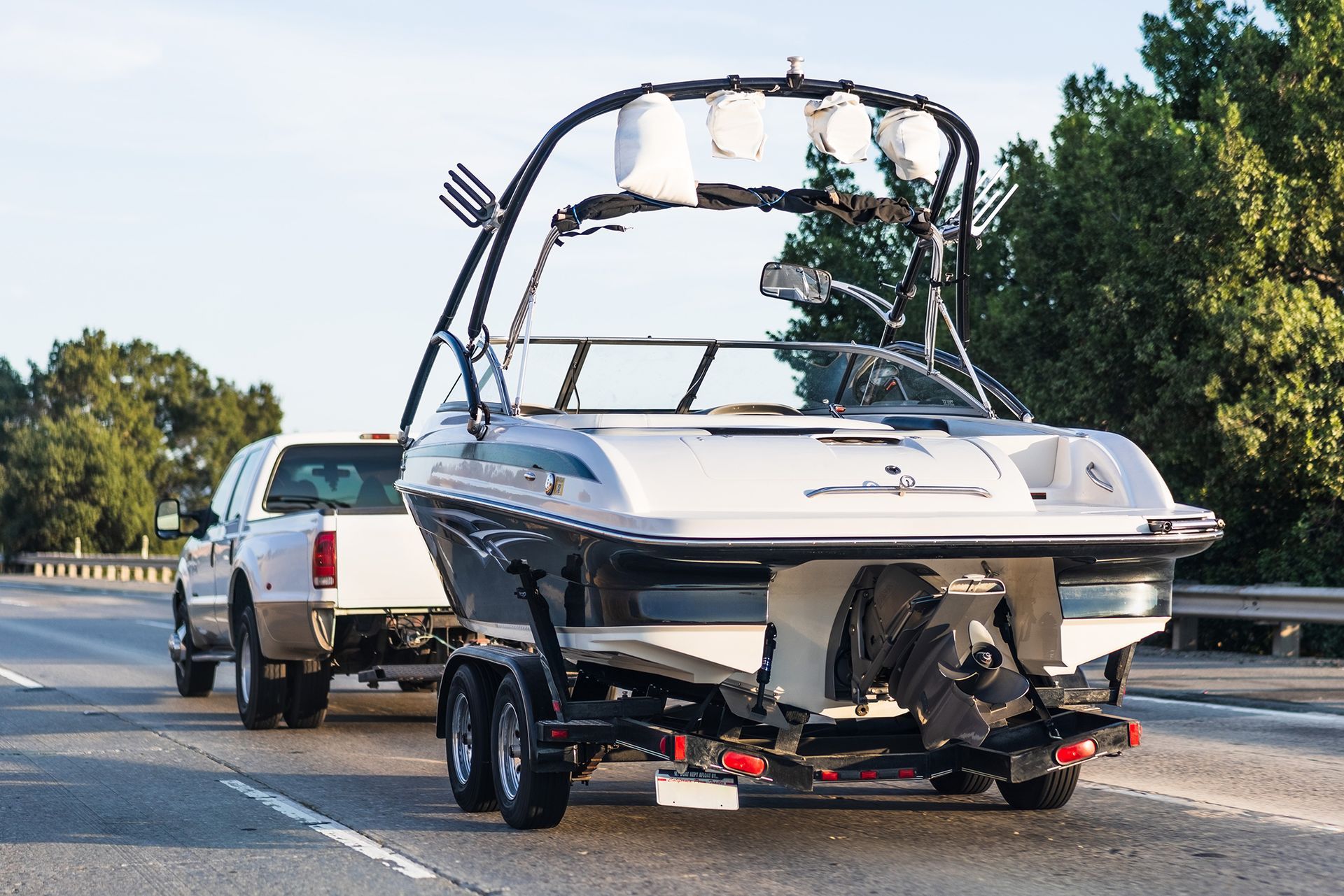 Boat on a trailer being towed by a white SUV on a highway under clear skies