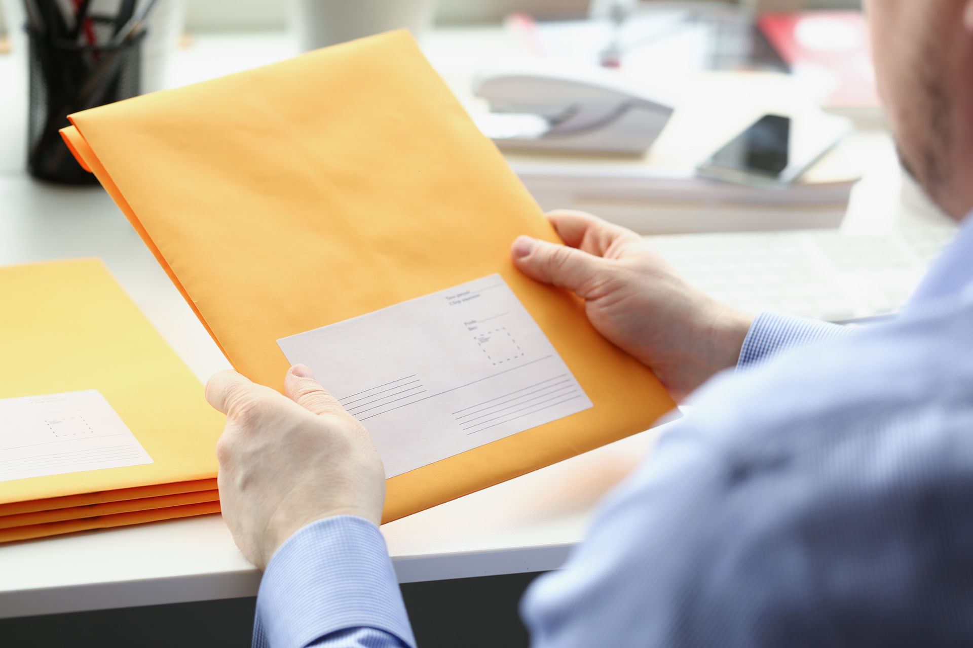 Hands holding an orange envelope with a white address label over a desk