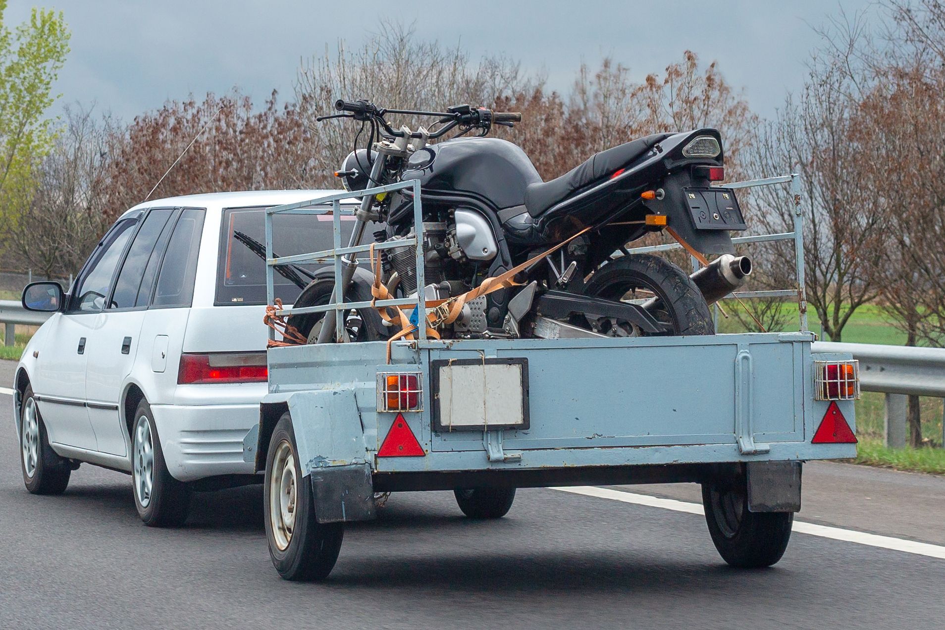 White SUV towing a light-blue trailer carrying a black motorcycle on a highway