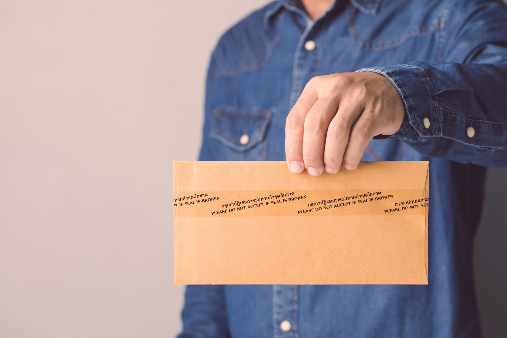 Person in a blue shirt holding a tan envelope with a handwritten address