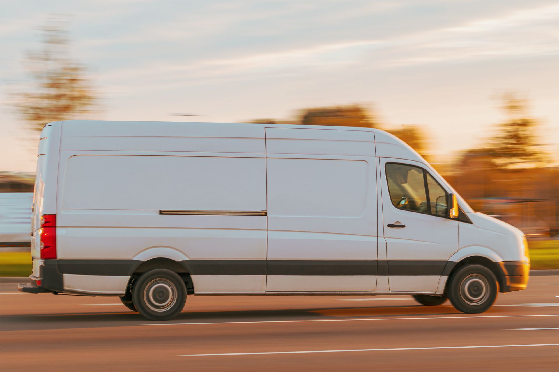 White delivery van driving on a road with motion-blurred background at sunset