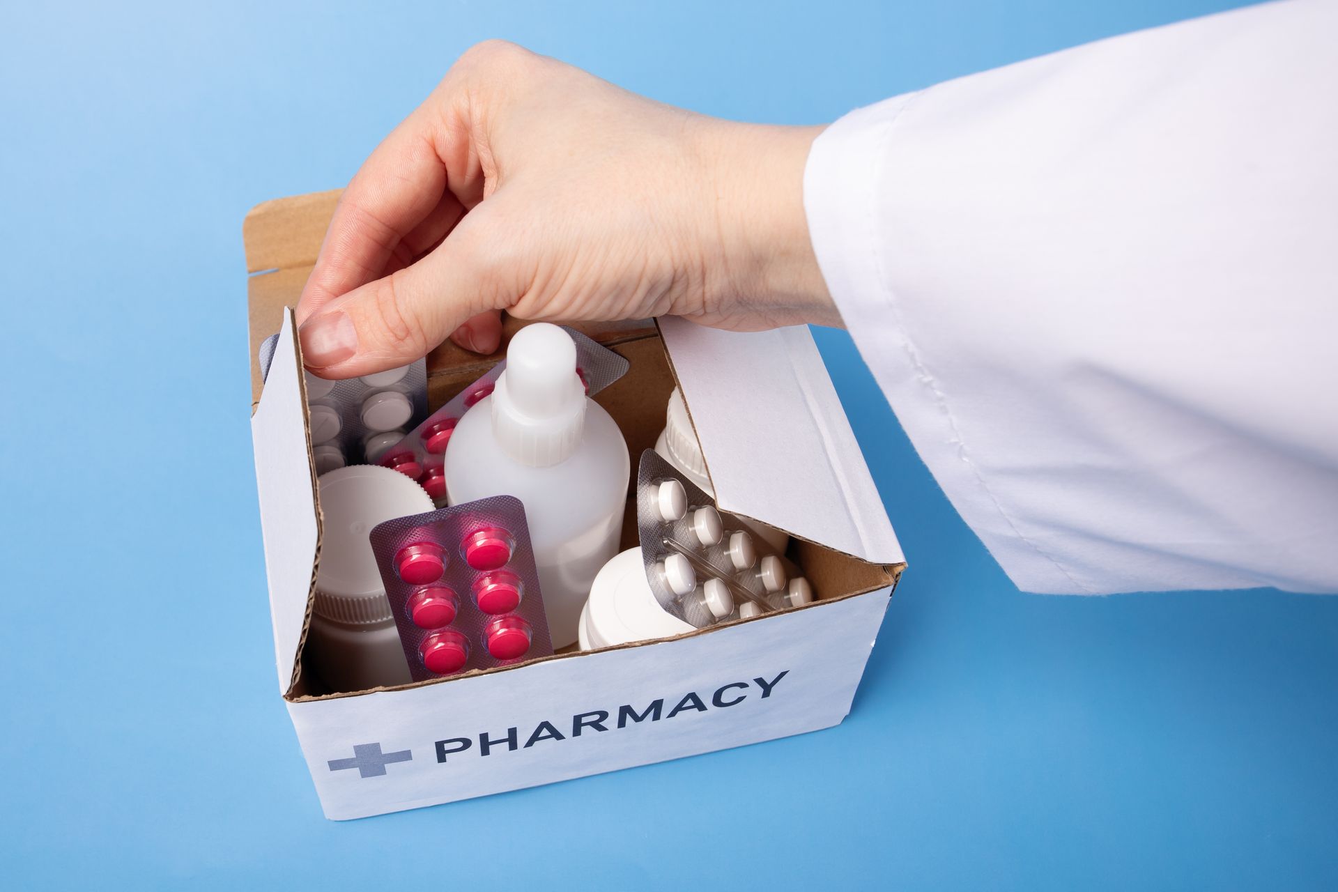 Hand placing medicine into a pharmacy box with pills and bottles on a blue background