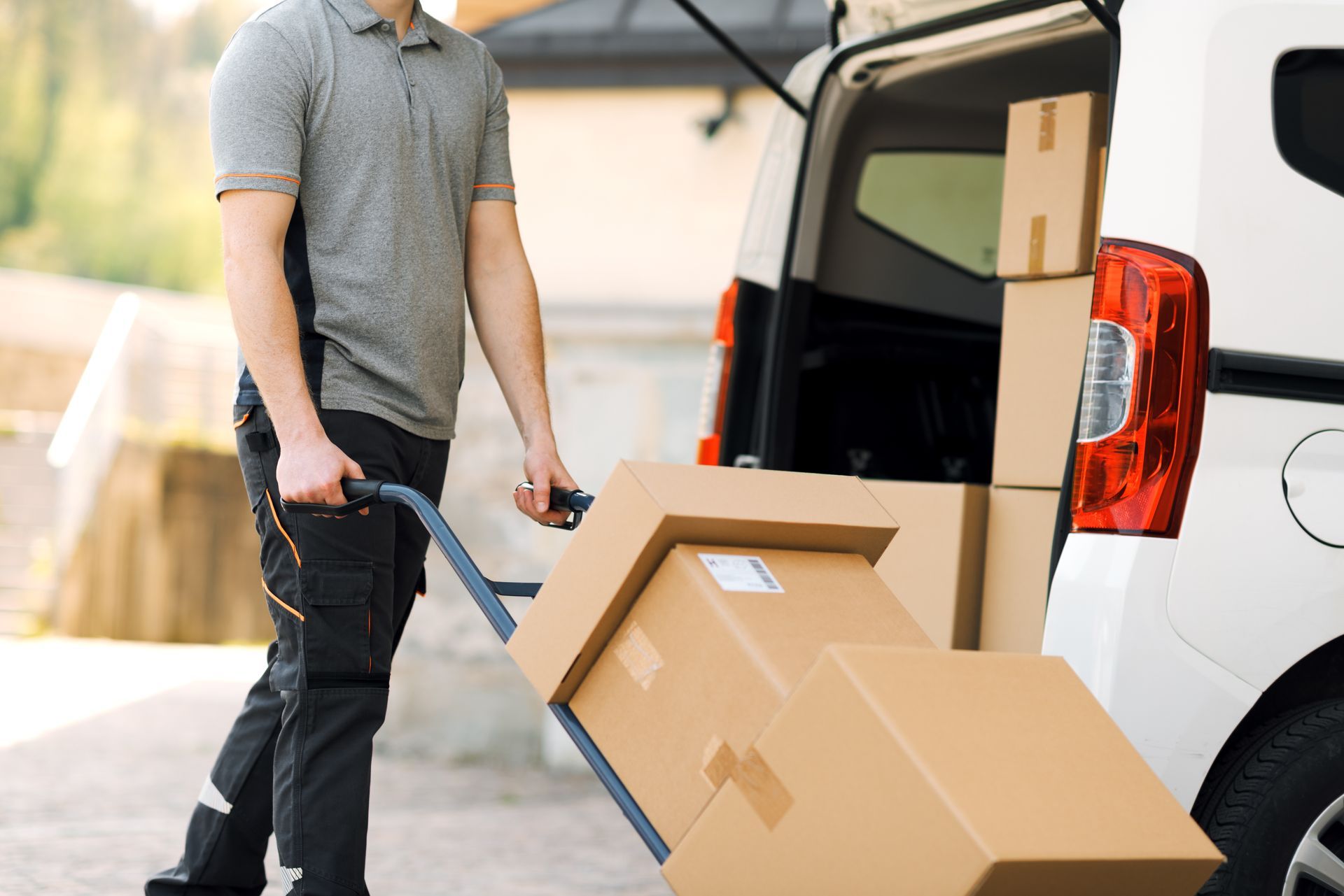 Person unloading cardboard boxes from a white van outdoors
