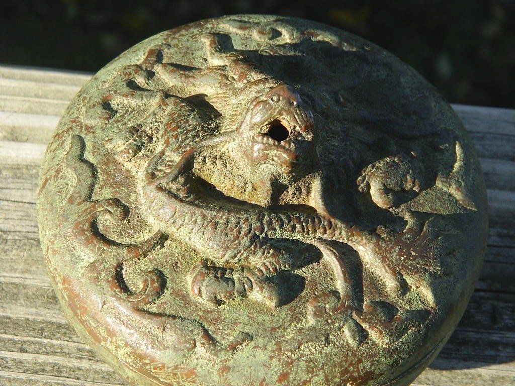 Round metal medallion with an embossed dragon design on a wooden surface