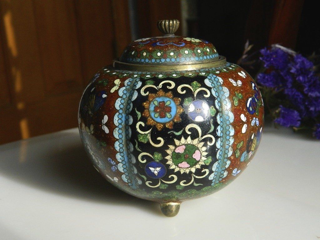 Ornate black ceramic jar with colorful floral inlay and a gold lid on a white surface