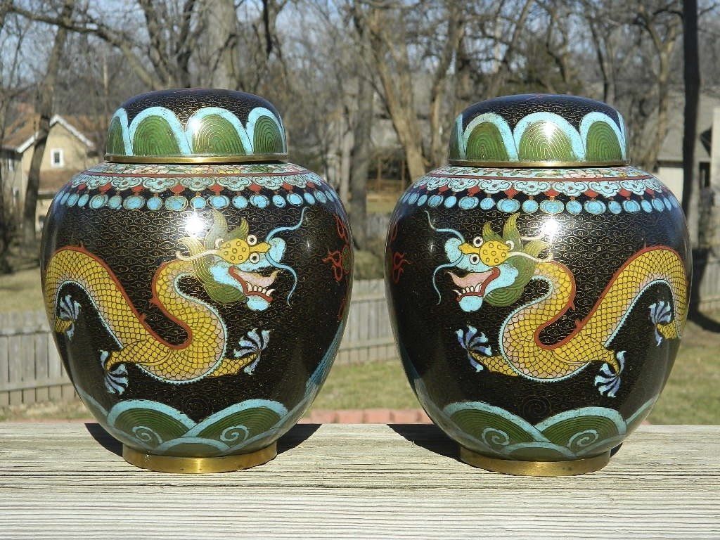 Two decorative black ceramic urns with colorful dragon designs displayed outdoors in a yard