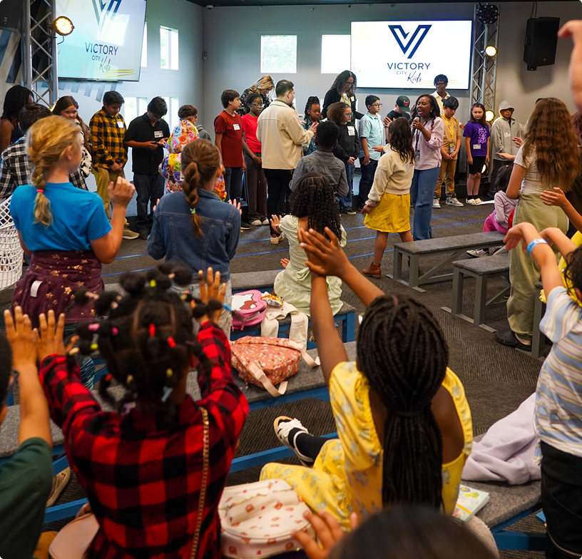 Crowd gathered in a church auditorium, facing speakers onstage with a Victory logo screen.
