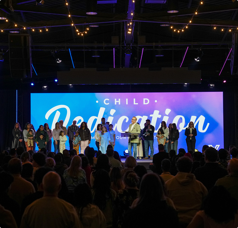 Children’s dedication ceremony on a stage with a large blue-lit screen and people standing in a line