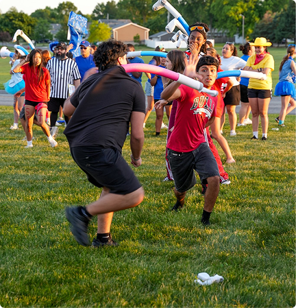 People playing a field game outdoors, with one person running and another swinging a pink bat.