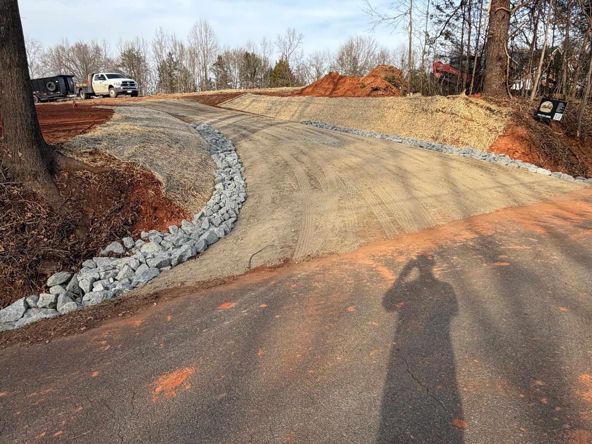 A newly landscaped driveway entrance featuring curved rock-lined drainage channels and cleared dirt leading to a road.