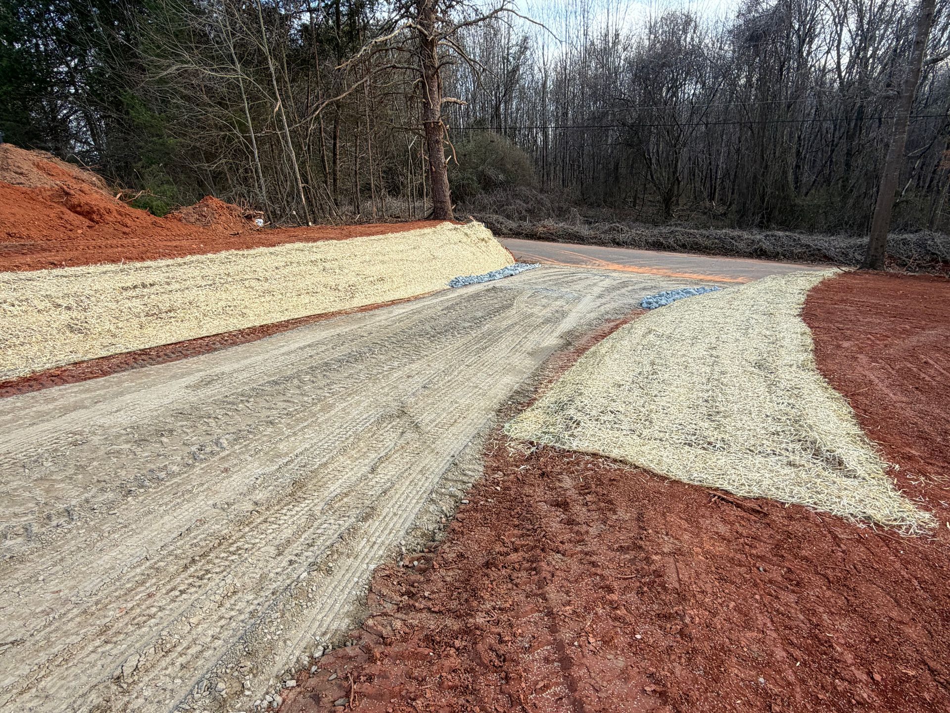 A gravel driveway entrance leading from a paved road, flanked by red clay soil and newly laid light-colored stone.