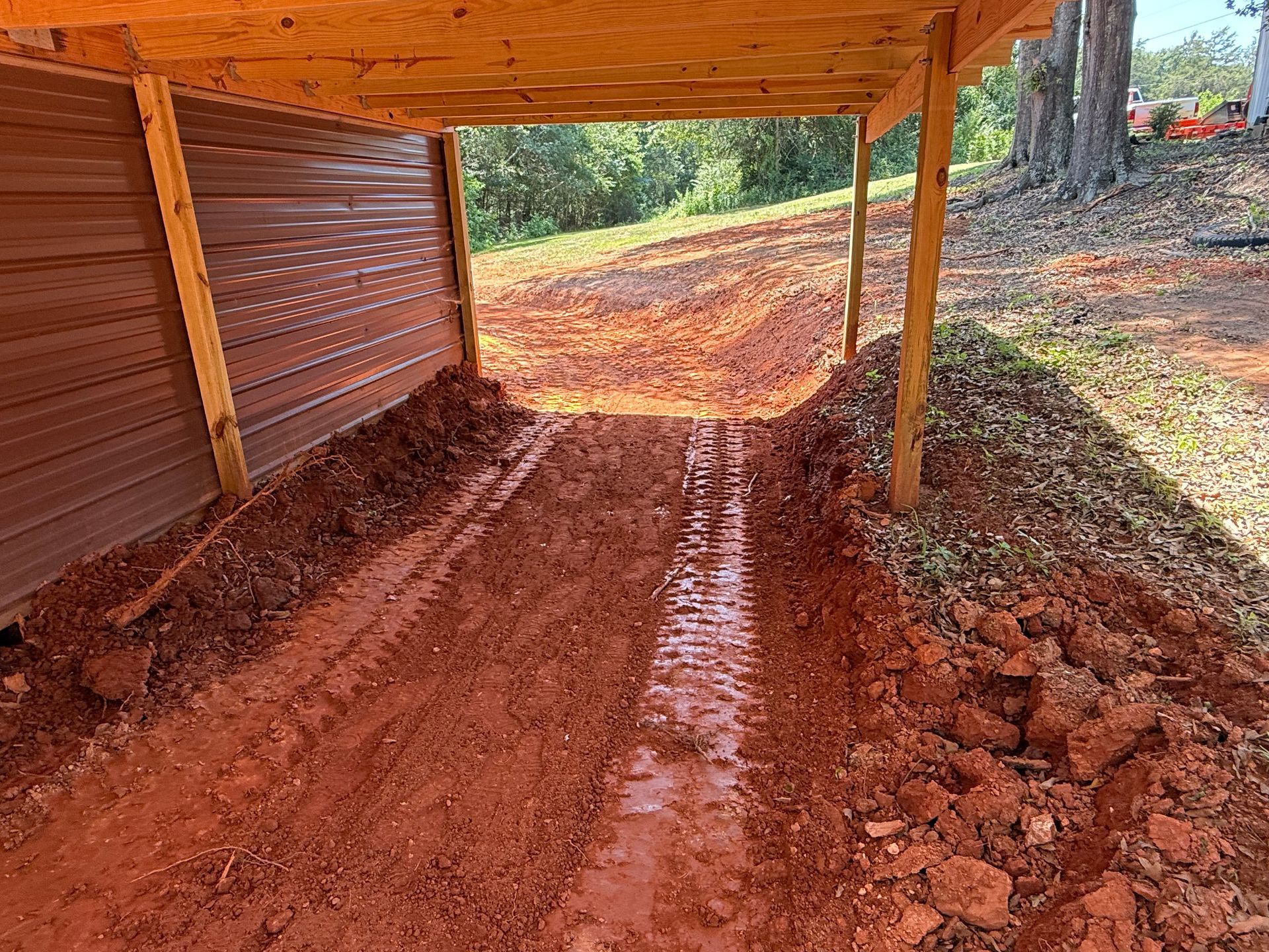 A red-clay track leads into a wooden, open-sided shelter with corrugated metal siding.