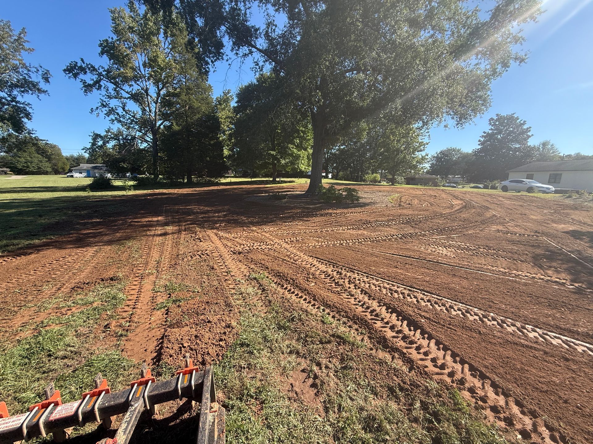 A view from a tractor looking over a newly cleared, muddy field with tire tracks and trees under a clear blue sky.
